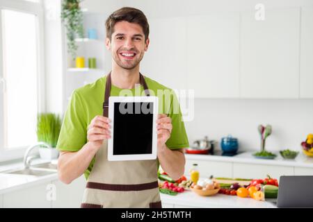 Portrait d'un sympathique type de cuisine à l'aide d'un appareil montrant l'écran à la maison cuisine à l'intérieur Banque D'Images