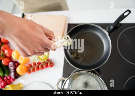 Photo rognée homme de cuisson ajoutant de l'huile sur la poêle Banque D'Images