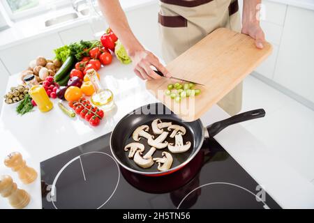 Photo de la poêle homme de cuisson en bois ajoutant des champignons de légumes tranchés sur une poêle Banque D'Images