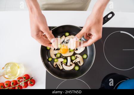 Photo de culture homme de cuisson ajoutant des légumes en tranches de champignons sur une poêle à frire faisant une omelette Banque D'Images