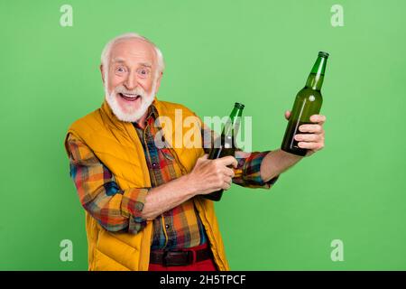 Photo d'un beau homme mûr excité habillé jaune gilet souriant tenant des bouteilles de bière isolé couleur verte fond Banque D'Images