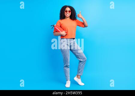 Photo du corps entier de la jeune femme afro sourire positif heureux montrer le pouce vers le haut fine garde de tir isolé sur fond bleu de couleur Banque D'Images