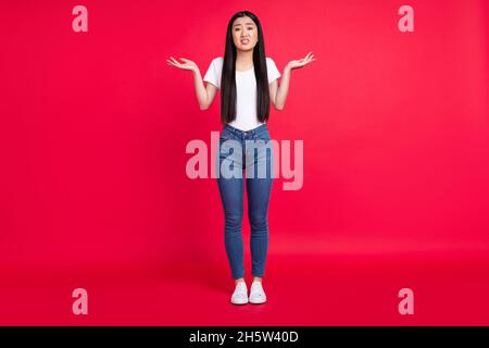 Photo de corps complet de jeune fille asiatique attrayante malheureux négatif haussement d'épaules cluless confus isolé sur fond rouge couleur Banque D'Images