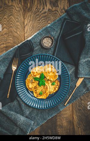 Petites crêpes aux herbes sur une assiette bleue sur fond de bois rustique, vue de dessus Banque D'Images