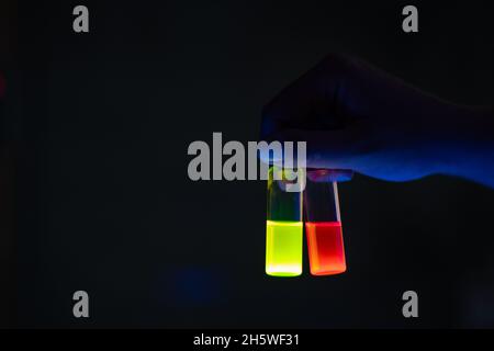 Une femme chercheuse tenant des flacons en verre de réaction photochimique dans un laboratoire organique - radioactif - fluorescence.Un espace de copie verso noir Banque D'Images