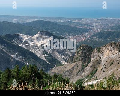 Vue sur les carrières de marbre de Carrare, les chemins sculptés sur le flanc de la montagne et la ville de Carrare et la côte en face. Banque D'Images