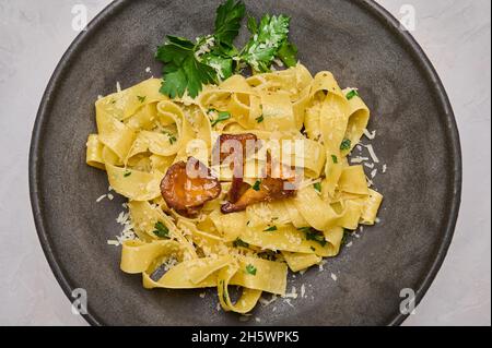 Gros plan sur les pâtes italiennes pappardelles aux champignons chanterelles, fromage et persil sur une assiette foncée, vue du dessus Banque D'Images