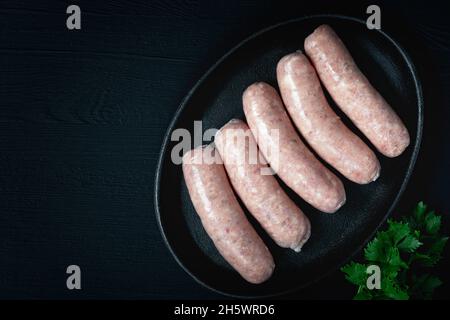Bouchers crus fraîchement préparés saucisses dans des peaux aux herbes sur une table en bois noir Banque D'Images