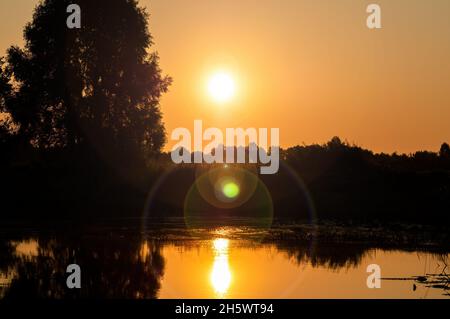 Orange soleil à l'aube sur la surface de l'eau du lac. Banque D'Images