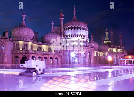 Le Pavillon Royal, Brighton, est éclairé par des illuminateurs LED de couleur derrière la patinoire d'hiver érigée dans les jardins du Pavillon.Brighton, East Sussex, Angleterre, Royaume-Uni.Préparation de la surface de la patinoire ce pour une autre session de patinage. Banque D'Images