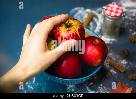 La main d'une femme atteint une pomme rouge mûre dans un bol. Choisir des fruits pour faire une tarte traditionnelle aux pommes de Thanksgiving. Ingrédients pour cuire à la maison Banque D'Images