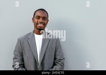 Souriant homme d'affaires afro-américain en costume formel souriant largement tout en se tenant sur fond gris et en regardant la caméra Banque D'Images