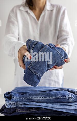 Cachez une femme anonyme en chemise blanche avec une pile de jeans bleus dans les mains Banque D'Images