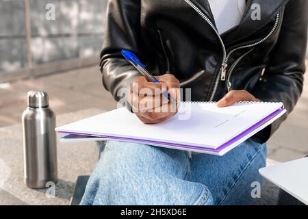 Anonyme Afro-américaine femme en cuir prenant des notes dans le carnet dans la rue près du bâtiment dans la ville Banque D'Images