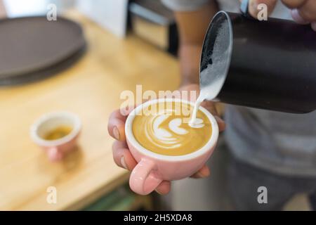 Un barista ethnique anonyme verse du lait dans une tasse avec du café tout en se tenant au comptoir avec une cafetière et de la vaisselle dans une maison de café Banque D'Images