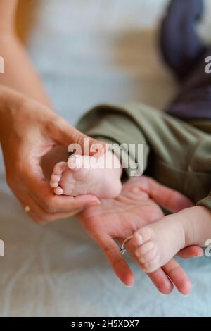 De dessus de la récolte mère anonyme massant de petits pieds d'adorable pieds nus bébé couché sur le lit dans le matin ensoleillé Banque D'Images