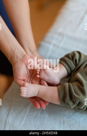 De dessus de la récolte mère anonyme massant de petits pieds d'adorable pieds nus bébé couché sur le lit dans le matin ensoleillé Banque D'Images