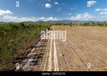 Un drone s'envola le long d'une piste de terre dans le Bush du pays sous un ciel bleu nuageux Banque D'Images