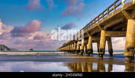 Le quai en bois historique de Tolaga Bay, lors d'une journée magnifique avec des reflets sur le sable humide Banque D'Images