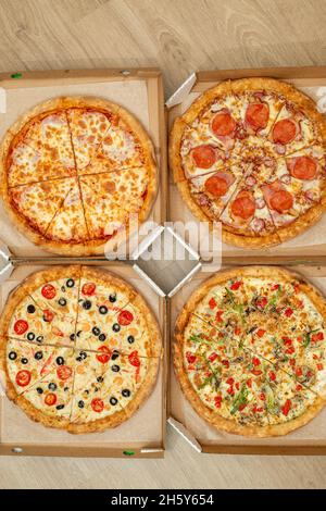 Quatre pizzas coupées différentes sont en boîtes carrées.Viande et pizza végétarienne.Vue de dessus.Photo verticale. Banque D'Images