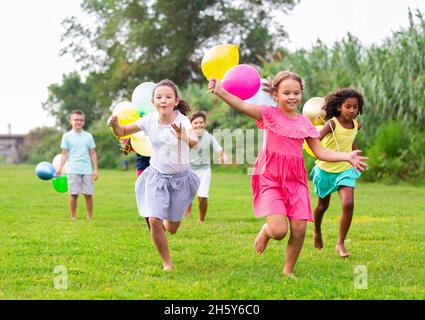 Joyeux préadolescents garçons et filles avec des ballons courir sur la pelouse verte Banque D'Images