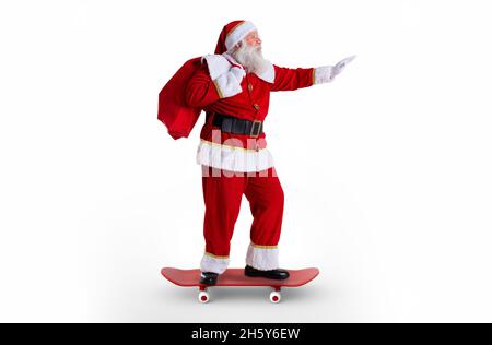 Le père Noël à bord d'un skateboard ou d'une longue planche et tenant un sac rempli de cadeaux sur fond blanc. Banque D'Images