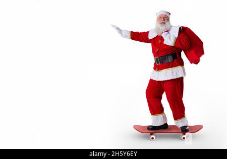 Le père Noël à bord d'un skateboard ou d'une longue planche et tenant un sac rempli de cadeaux sur fond blanc. Banque D'Images