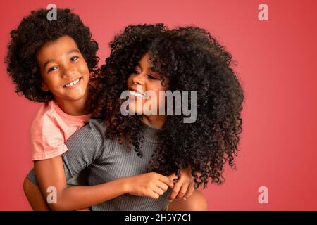 Portrait d'une jeune mère afro-américaine avec un tout-petit fils.Arrière-plan rouge.Famille brésilienne. Banque D'Images