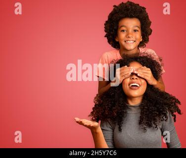 Un garçon afro-américain tenant sa mère fermée les yeux.Arrière-plan rouge.Fête des mères.Famille brésilienne. Banque D'Images