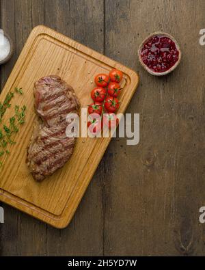Steak de stripine grillé avec tomates cerises, thym et sauce aux baies sur planche à découper en bois.Délicieuse viande juteuse et tendre.Verticale, vue de dessus Banque D'Images