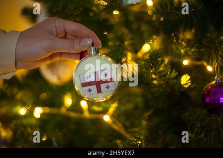 Une fille porte une décoration sur un arbre de Noël avec le drapeau de la Géorgie Banque D'Images