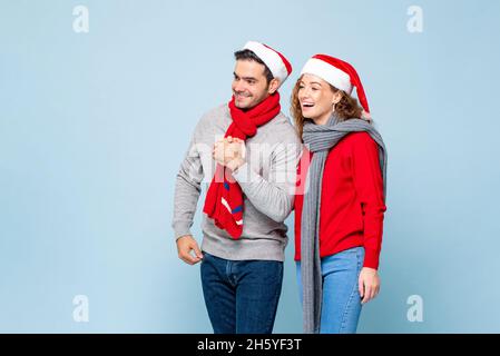 Portrait d'un couple caucasien heureux en tenues de Noël tenant les mains l'une de l'autre sur fond de studio isolé bleu clair Banque D'Images