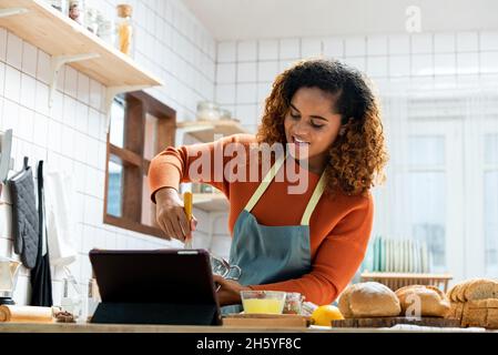 Jeune femme afro-américaine en streaming vidéo en direct enseignement de la cuisine de boulangerie en ligne dans la cuisine à la maison Banque D'Images