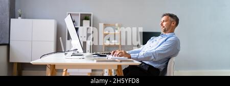 Homme assis en mauvaise posture working on Computer in Office Banque D'Images