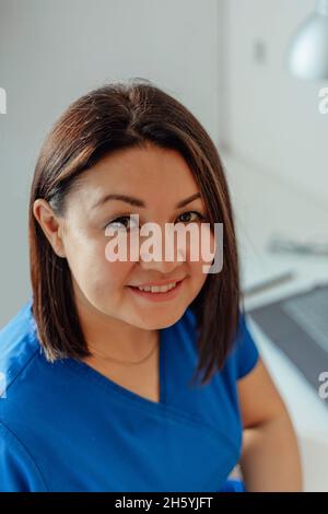 portrait d'une femme médecin heureuse assise à une table avec un ordinateur portable en uniforme souriant à l'appareil photo Banque D'Images