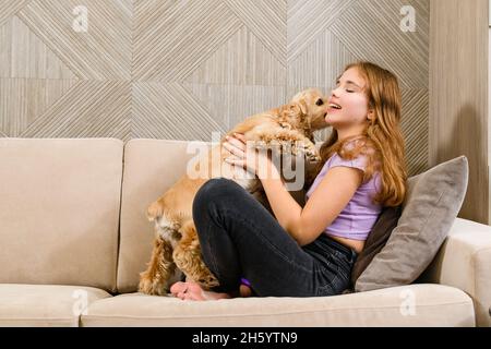 Adolescente jouant avec un spaniel tout en étant assise sur un canapé dans le salon.Elle embrasse son chien tout en étant assise sur un canapé. Banque D'Images