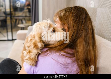 Adolescente jouant avec un spaniel tout en étant assise sur un canapé dans le salon.Elle embrasse son chien tout en étant assise sur un canapé. Banque D'Images