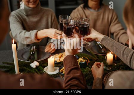 Gros plan de quatre amis qui dégustent un dîner de Noël ensemble et qui toaster avec des verres à vin tout en étant assis près d'une table à manger élégante avec des bougies Banque D'Images