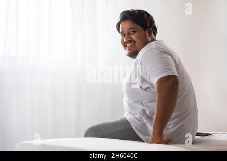 Un gros homme souriant assis dans sa chambre. Banque D'Images