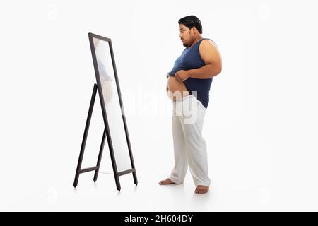 Portrait d'un gros homme regardant le bellyfat dans le miroir avec surprise sur fond simple. Banque D'Images