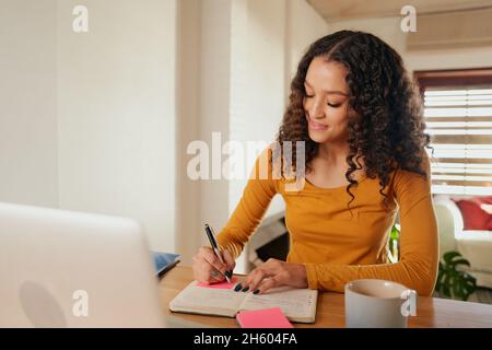 Happy Multi-cultural femmes focalisées, écrivant dans le carnet.Jeune professionnel travaillant à distance avec un ordinateur portable dans un appartement moderne Banque D'Images