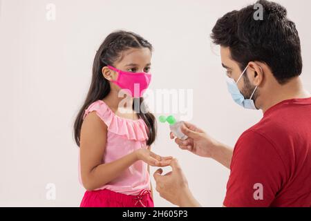 UN PÈRE DONNE DE L'ASSAINISSEUR POUR LES MAINS À SA FILLE PORTANT UN MASQUE FACIAL Banque D'Images