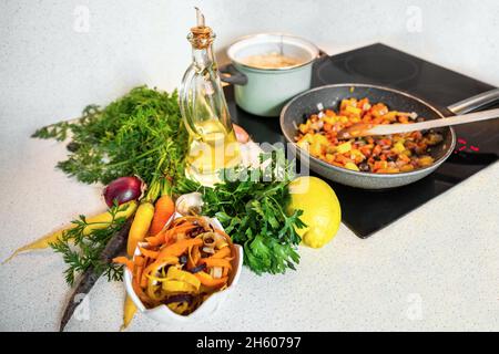 Préparation de la soupe aux carottes.Carottes entières et pelées crues colorées, oignons, citron et huile sur le plan de cuisine, émincées de carottes sur la poêle et en pot avec bouillon. Banque D'Images