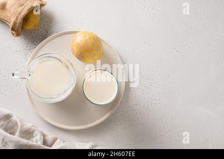 Lait de pomme de terre vegan en verre et pomme de terre dans un bol sur fond clair.Gros plan.Produit de remplacement du lait à base de plantes et sans lactose. Banque D'Images