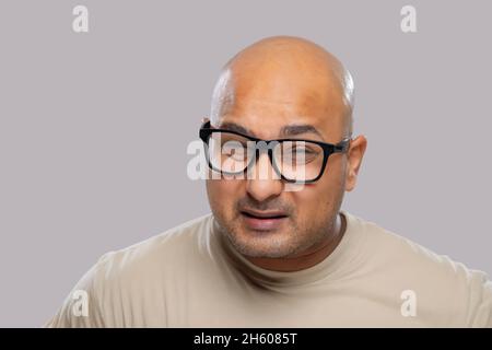 Portrait d'un homme chauve portant des lunettes avec expression confuse sur fond Uni. Banque D'Images