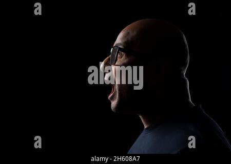 Portrait d'un homme à tête blanche portant des lunettes qui hurlent sur fond noir foncé. Banque D'Images