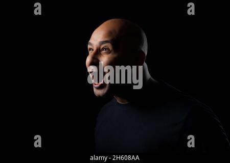Portrait d'un homme chauve criant sur fond noir foncé. Banque D'Images