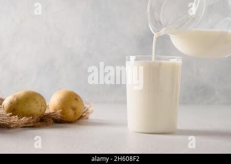 Verser le lait de pomme de terre vegan dans le verre et la pomme de terre dans le bol sur fond clair.Gros plan.Produit de remplacement du lait à base de plantes et sans lactose. Banque D'Images