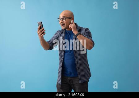 Portrait d'un homme chauve avec bluetooth dans ses oreilles appels vidéo sur téléphone mobile. Banque D'Images