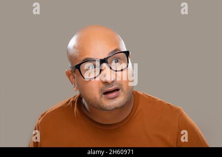 Portrait d'un homme chauve portant des lunettes avec expression confuse sur fond Uni. Banque D'Images